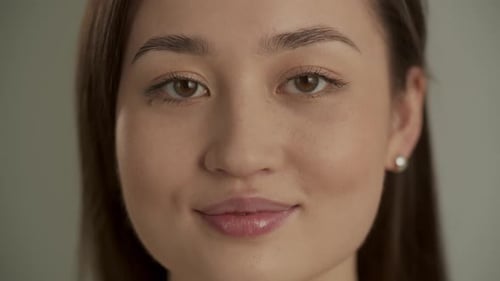 Front View of Pretty Asian Girl Looking at Camera with Smile and Blinking Isolated on Beige