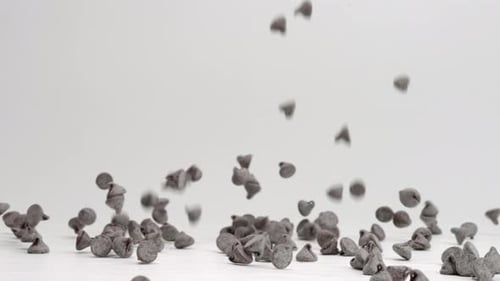 Semi sweet chocolate chips falling and bouncing into pile on white table top in slow motion