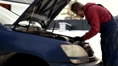 On the street near a country house a man is repairing his car