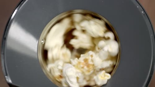 Slow motion overhead view: Popcorn kernels spin and pop in hot air popper.