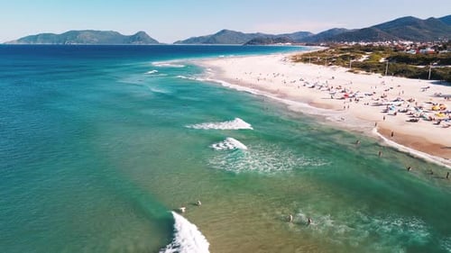 Aerial view of the sea with gentle waves and sandy beach with people relaxing on it