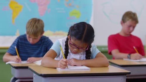 Students Sitting at Desks Writing in School Classroom Asian