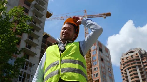 Unteransicht des glücklichen gutaussehenden jungen kaukasischen Baumeisters, der im Freien steht und den gelben Helm auszieht