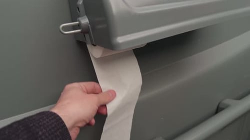 Nahaufnahme einer offenen Szene mit der Hand auf dem Toilettenpapierhalter, in der Öffentlichkeit eine Person zeigt, die eine Papierrolle zieht