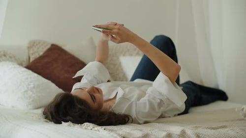 Happy Woman Lying on Bed Using Smartphone