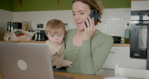 Woman Talking on Phone Holding Baby in Kitchen