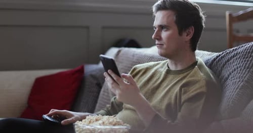 Man Relaxes on Couch, Using Phone and Eating Popcorn