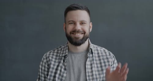 Smiling Man Waving in Front of Gray Background