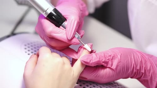 Close-up of a girl doing a manicure in a beauty salon. Nail care. Manicurist in pink gloves removes