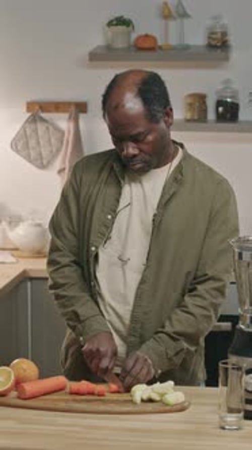 Vertical of Senior African American Man Cutting Carrot for Smoothie in Kitchen