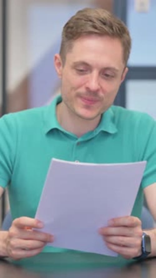 Man Reading Documents and Smiling in Modern Office