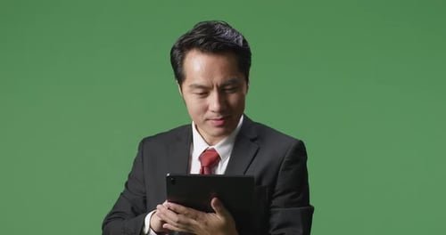 An Asian Business Man Smiling While Using Tablet On Green Screen Background In The Studio