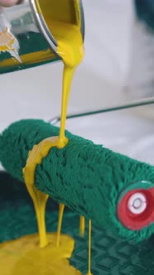 Builder Pours Yellow Paint Onto Roller Above Tray Closeup