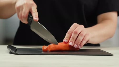 Woman Dicing Carrot on Cutting Board in Kitchen