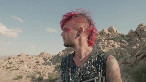 Punk male looks around and up, searching for something in a desert barren landscape.