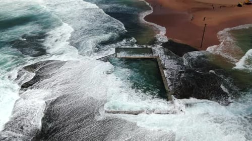 SLOW MOTION Aerial shot of waves and powerful ocean swell crashing over Monavale Rock Pool on a beau