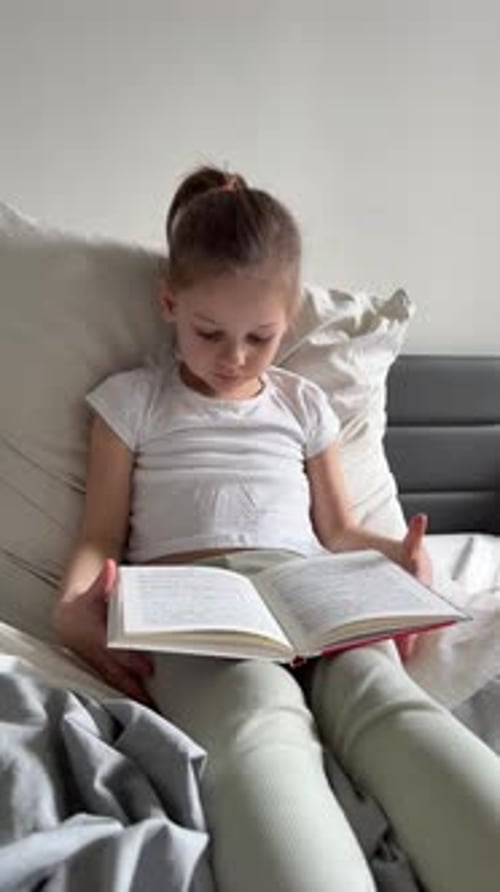 Little Girl Sitting on Her Parents Bed and Reading a Book in the Bedroom Concept of Quiet Time