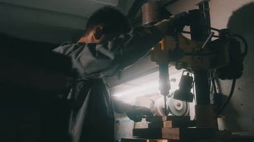 A worker works on a metal drilling machine in a workshop