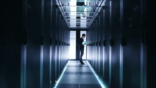 Un
ingeniero de TI masculino trabaja en una computadora portátil en un centro de Big Data. Se ven filas de servidores en rack.