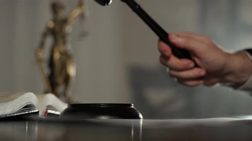 Closeup of a Judge Striking a Wooden Gavel on Desk with the Statue of Justice in the Background