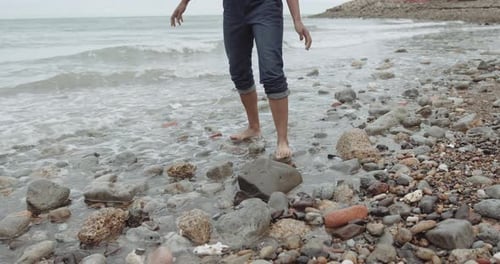 Close up of barefoot female feet in sea stepping on stones at beach