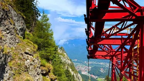 View from inside a red cable car gondola. The metal structure frames a steep rocky