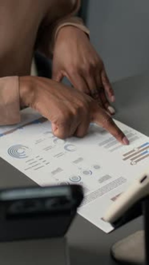 African American Woman Reading Business Document With Charts At Table