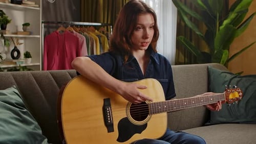 Woman Plays Acoustic Guitar and Sings on Sofa