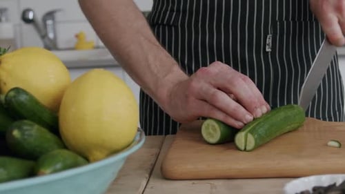 Person Slicing Cucumber in Kitchen with Silver Knife