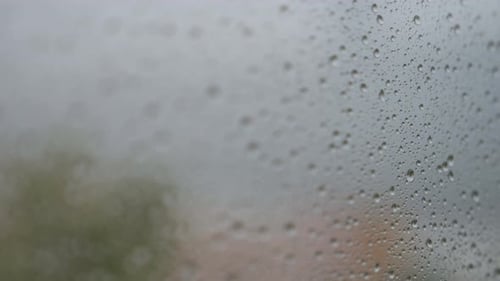 Narrow focus view and close-up of rainy glass as rain drops are seen on a window during gloomy and o