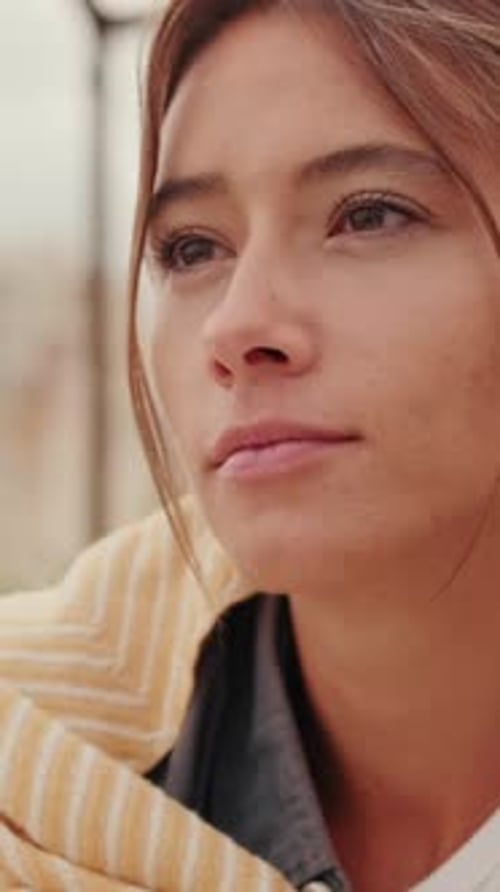 Vídeo vertical, primer plano de una mujer joven envuelta en una manta, sentada en un balcón