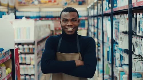 Portrait of African American Worker Man with Arms Crossed Standing By Shelves in Store