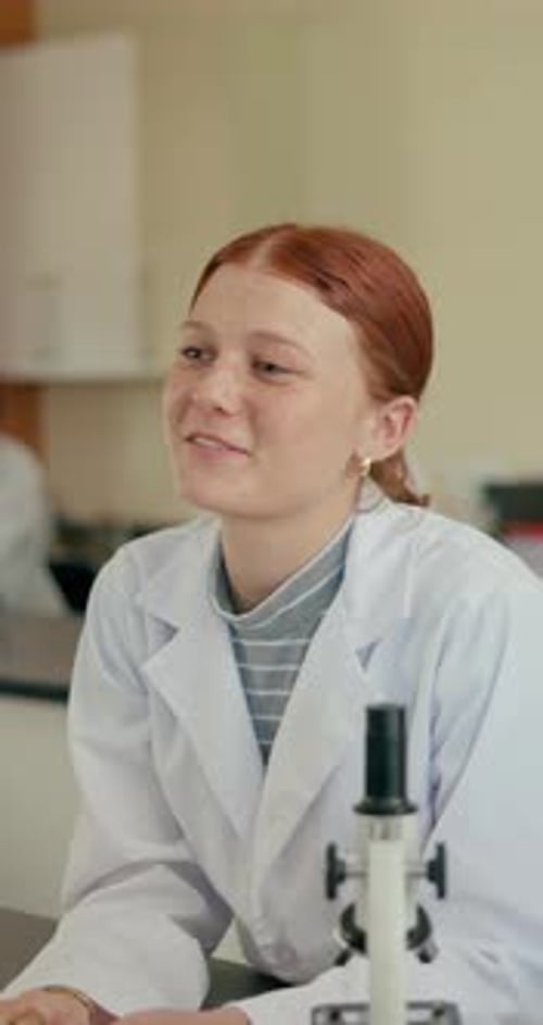 Teen student in lab coat raising hand in class