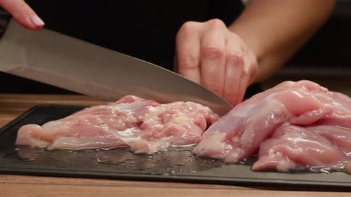 Homme tranchant un filet de dinde ou de poulet cru sur une planche à découper en chêne, cuisine en gros plan avec un couteau
