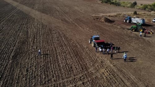 Aerial View of Adults Gathering Near Tractors in Field