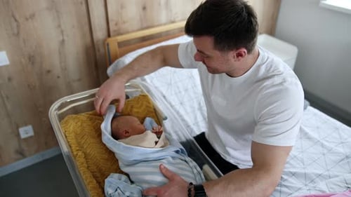 Loving Father Attending to Newborn Infant in Bassinet