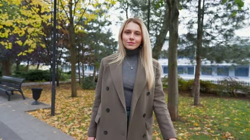 Attractive Business Woman with Blond Hair Walks in Autumn Park on Cloudy Day