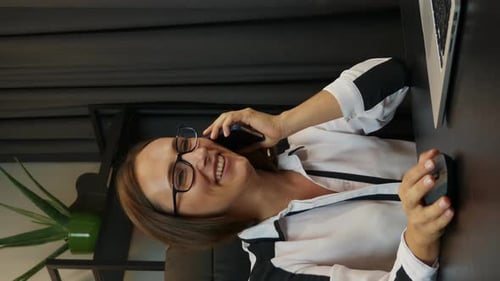 Woman talking on smartphone in front of laptop in modern office. Vertical video