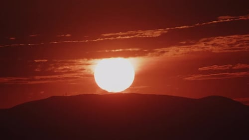 Extreme Nahaufnahme einer roten Sonne, die über einem Hügel aufgeht (Zoom im Zeitraffer)