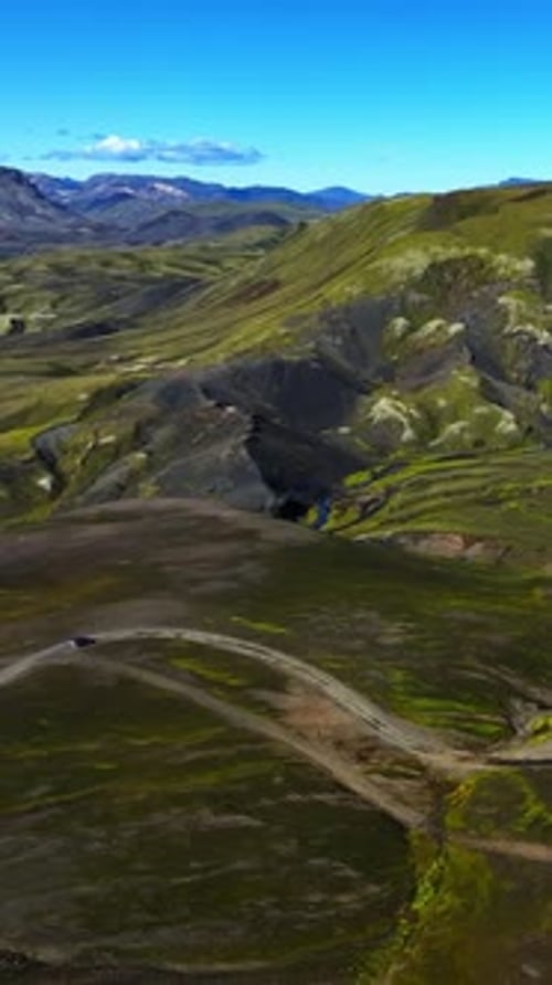Vertical drone view of an SUV driving along a winding dirt road through Icelandic highlands, with