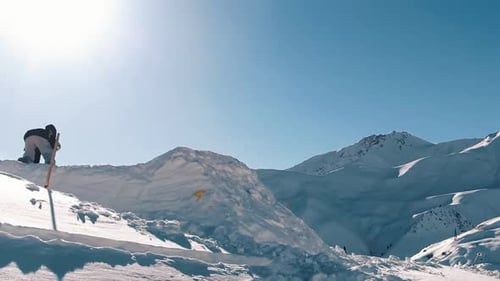 ZEITLUPE, Drohnenaufnahme, Weitwinkel: Profi-Snowboarder springt im Neuschnee und sprüht Schneeflocken über die Sonne.
