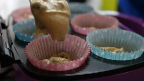 Adding cake mixture to paper cupcakes trays for baking