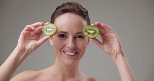 Woman Smiles and Holds Kiwi Slices Over Eyes