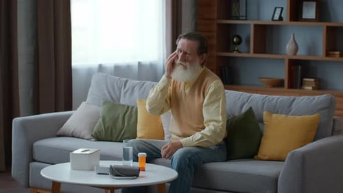 Senior Bärtiger Mann, der zu Hause an Fieber leidet und sein schwitzendes Gesicht mit Tissue Tracking Shot abwischt