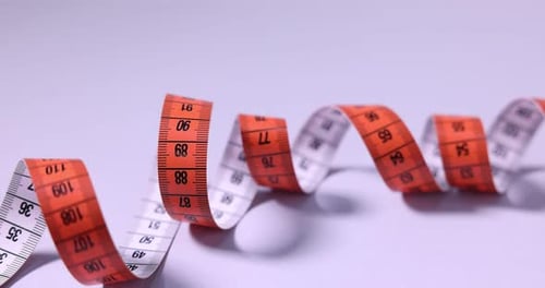 Orange and White Measuring Tape Spiraling on White Surface