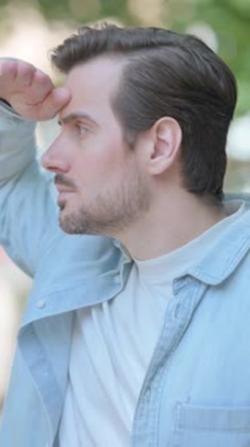 Man Shields Eyes, Looks at Watch Outdoors