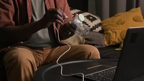 Man Uses Inhaler while Sitting on Couch