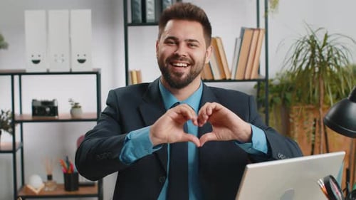 Smiling Man Makes Heart Gesture in Office