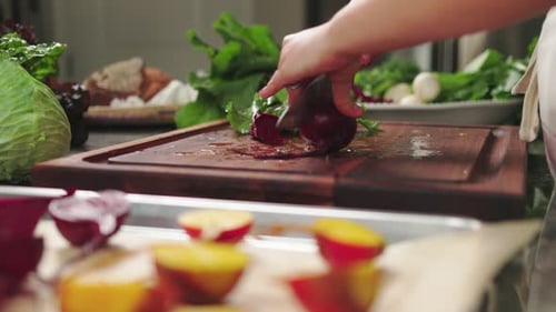 Person slicing fresh beetroot and leafy greens on a wooden board in a cozy kitchen