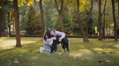 Female Affectionately Embraces Dog at Walk on Park Lawn